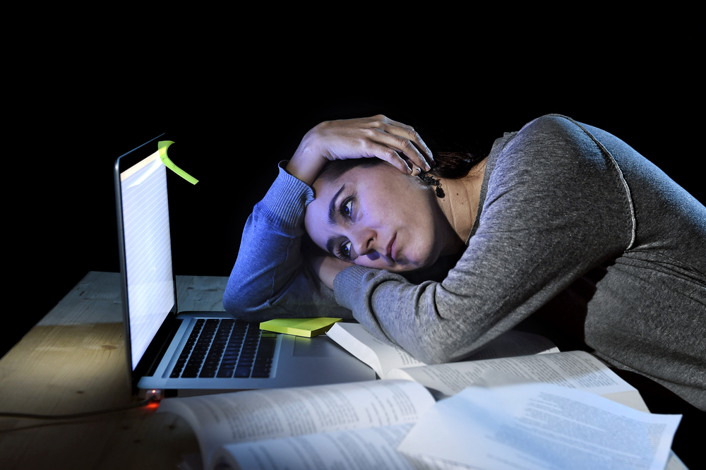 photograph of college student stressing over books and laptop