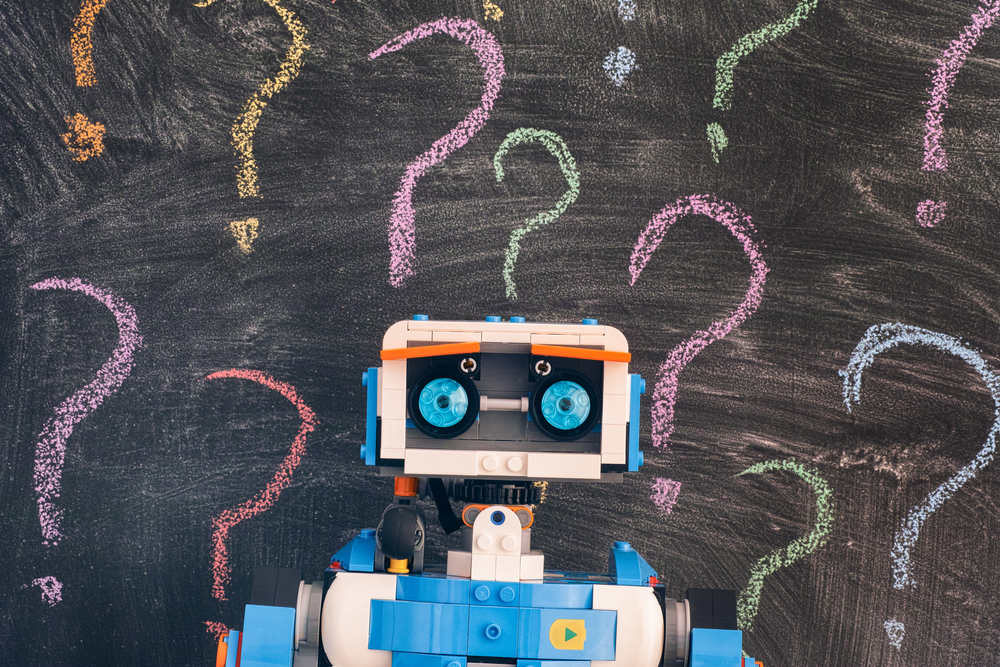 photograph of robot in front of chalkboard littered with question marks