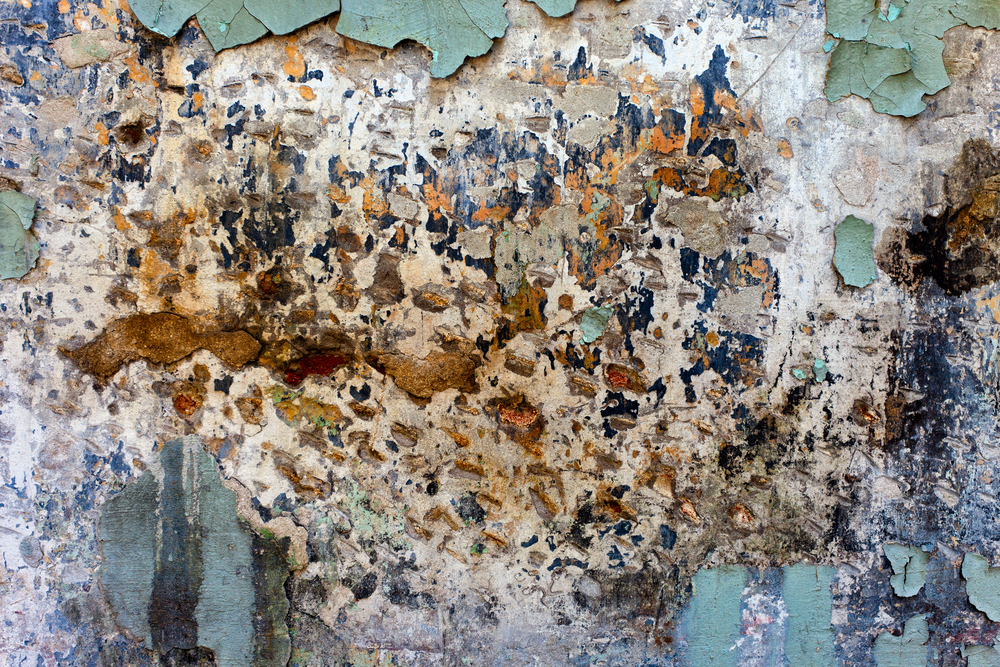 photograph of cracked brick wall with several different colors of peeling paint