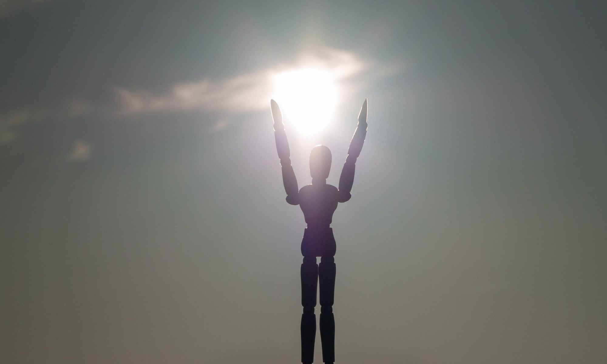 photograph of wooden figurine arms outstretched to sun
