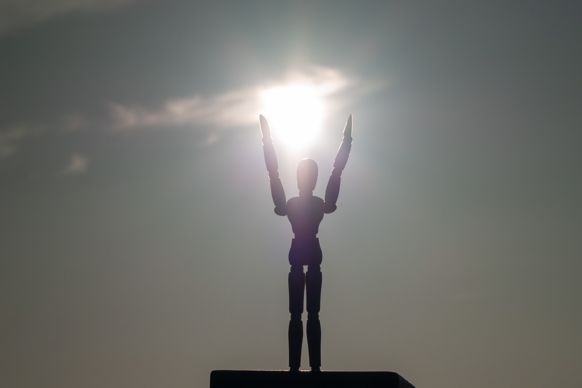 photograph of wooden figurine arms outstretched to sun