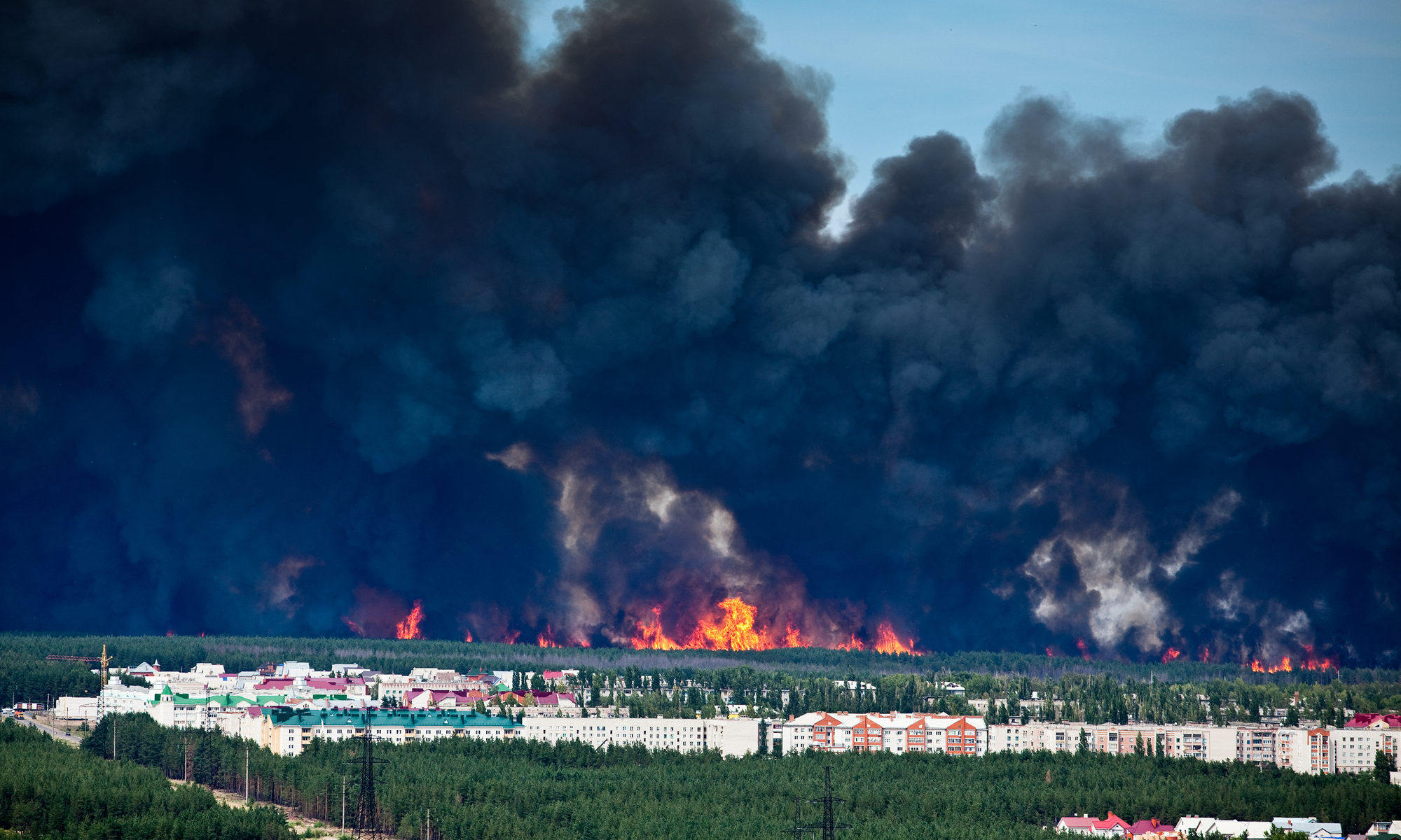 photograph of black smoke and forest fire approaching apartments