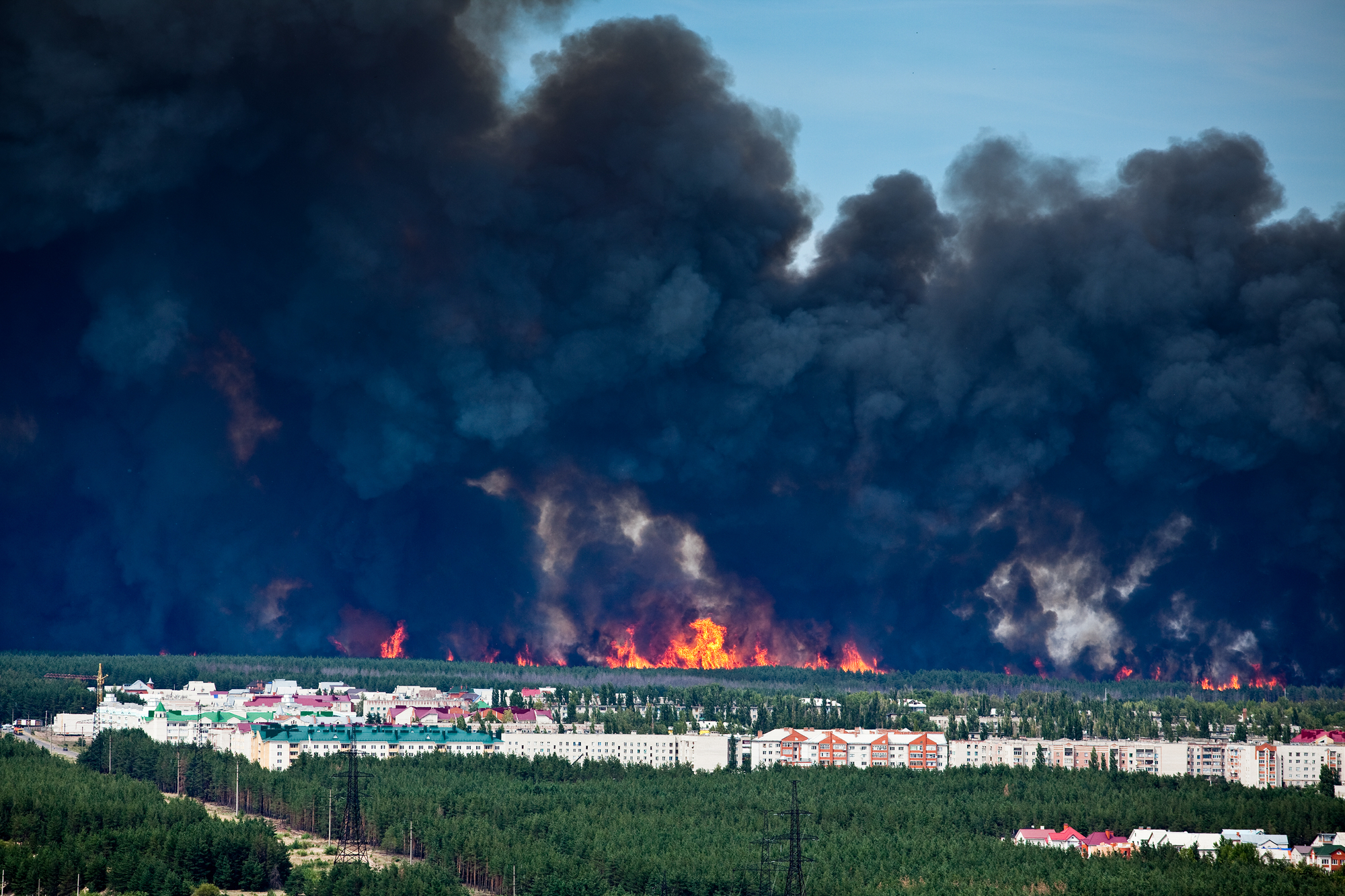 photograph of black smoke and forest fire approaching apartments