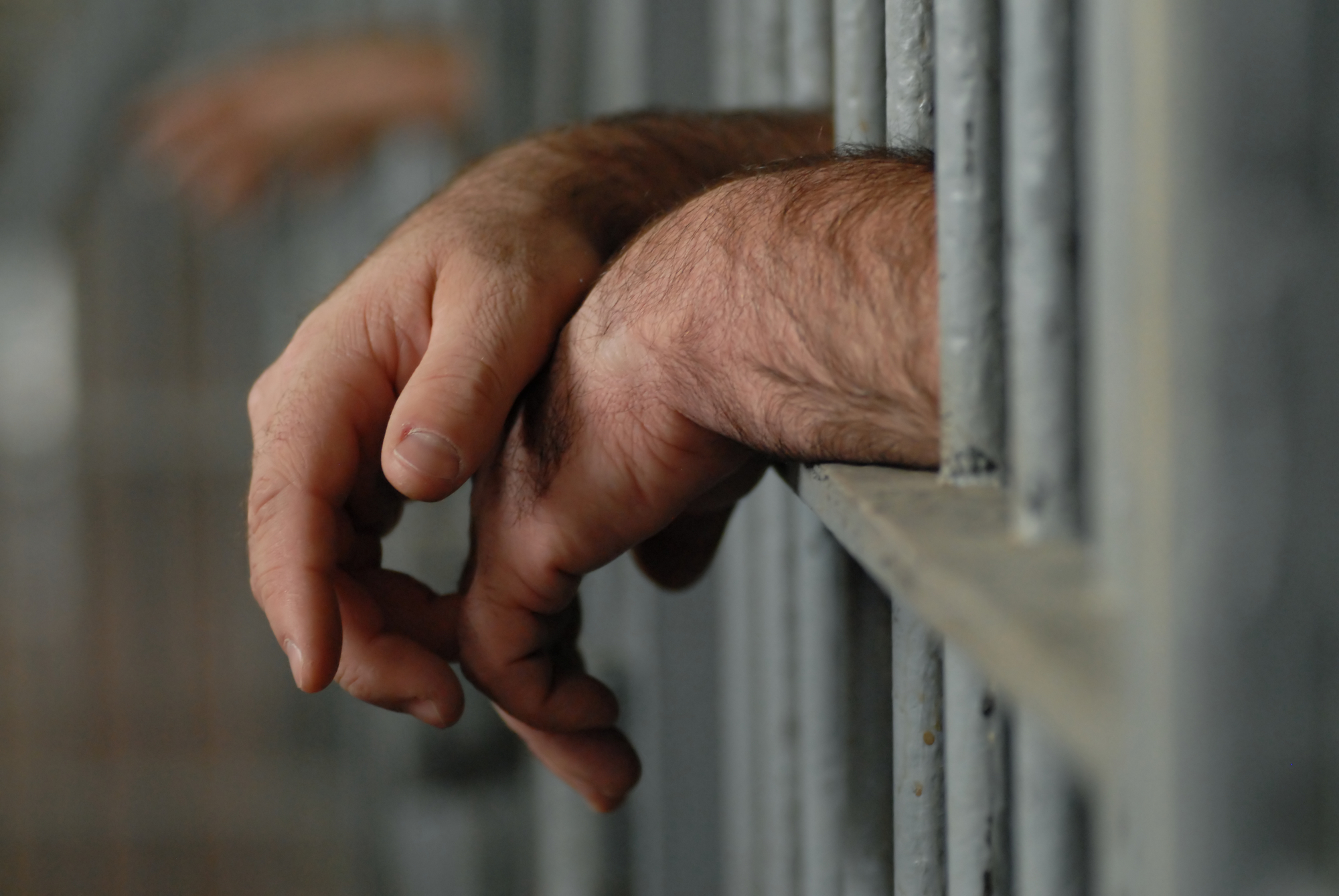 photograph of jail cell with man's hands hanging past bars