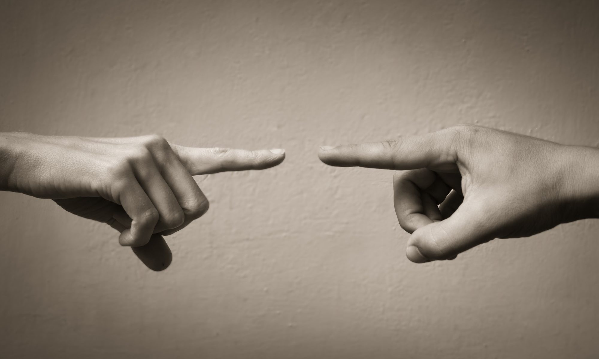 photograph of two hands pointing fingers at one another
