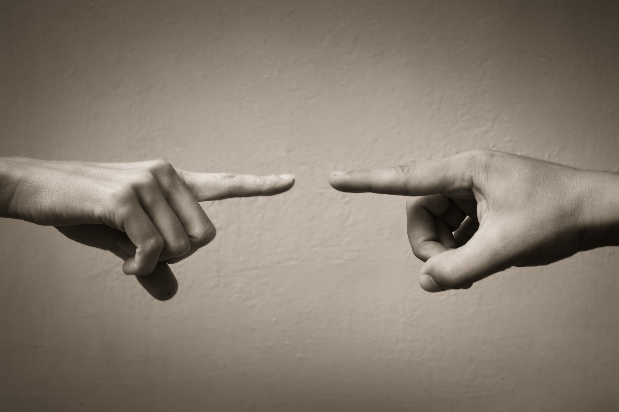 photograph of two hands pointing fingers at one another