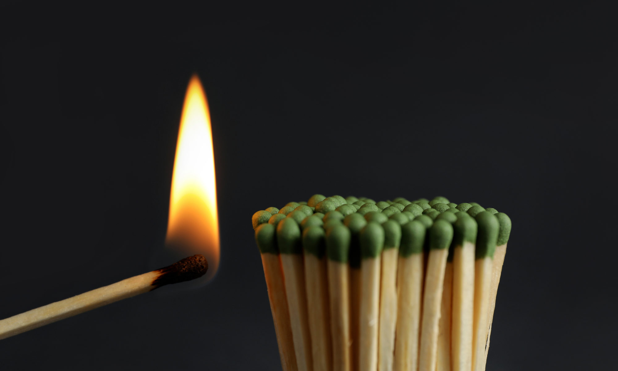 photograph of burning match near a bunch of unlit matches