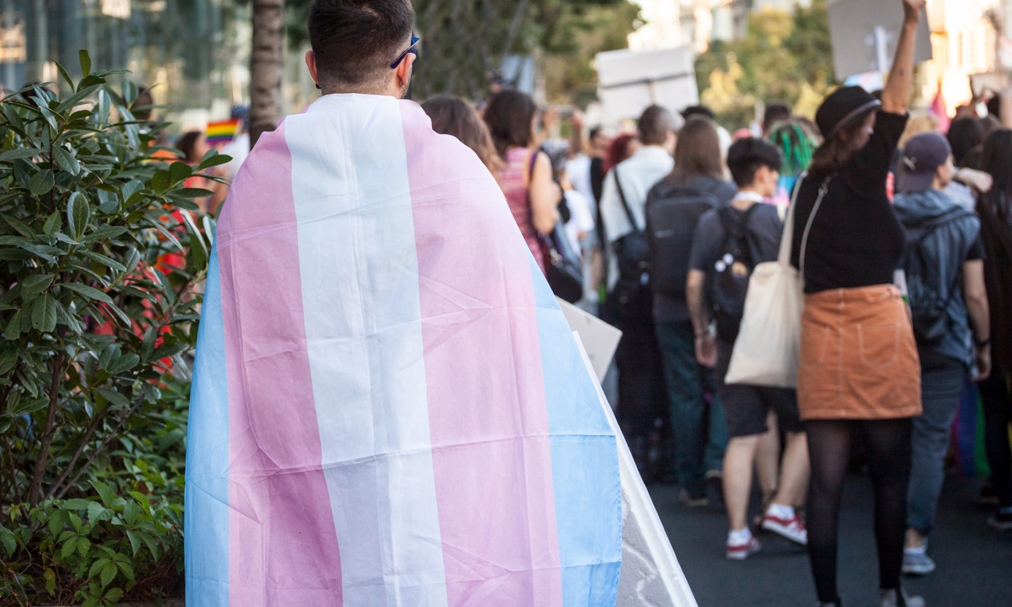 photograph of person walking through crowd draped in transgender flag
