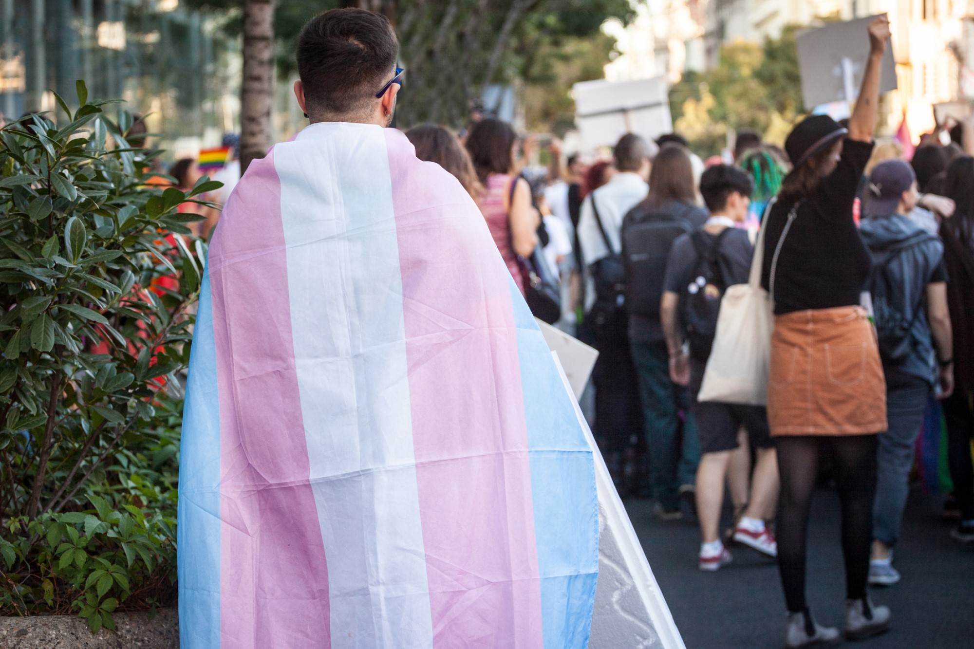 photograph of person walking through crowd draped in transgender flag