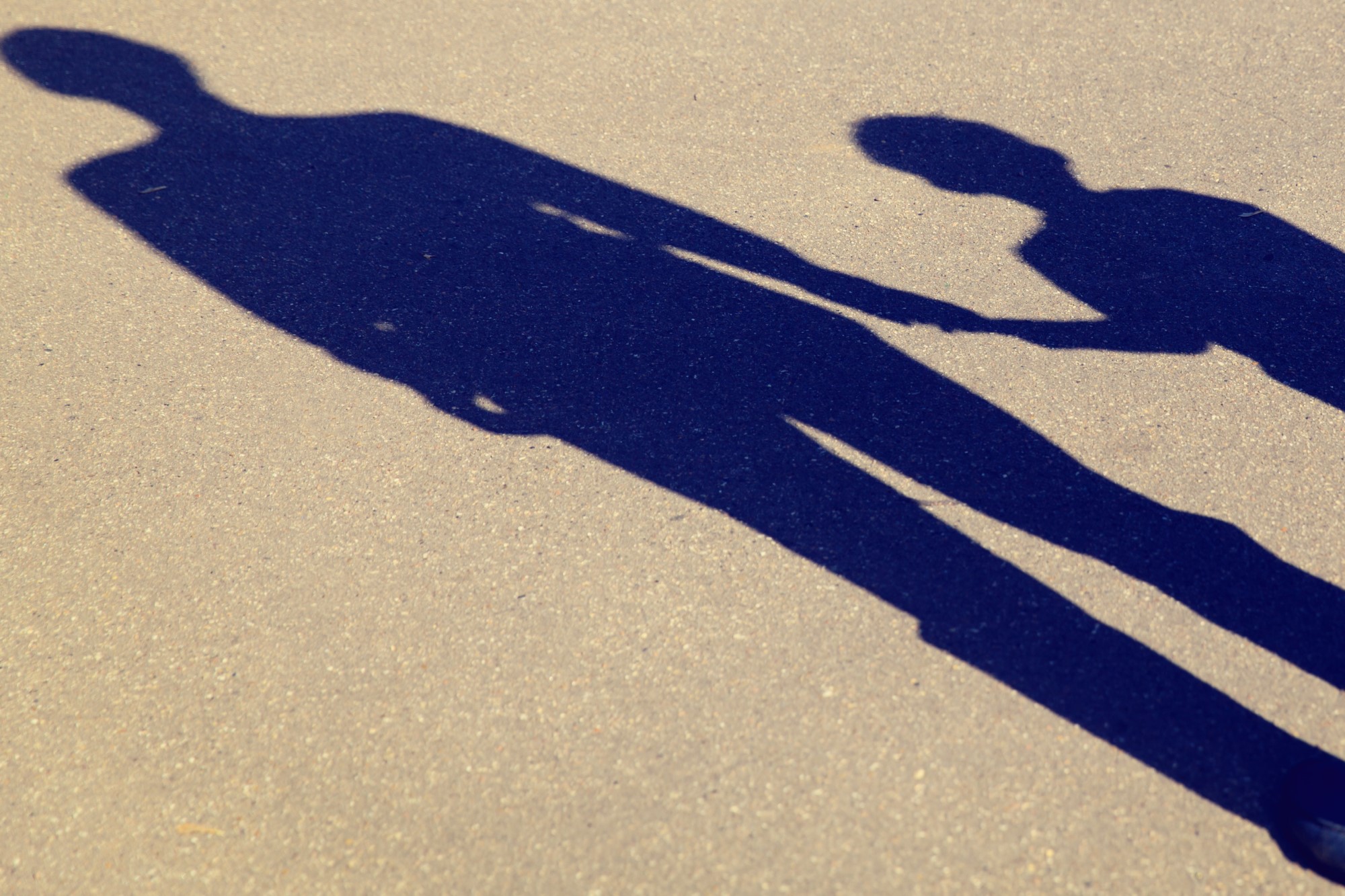 photograph of shadow on asphalt of parent holding child's hand