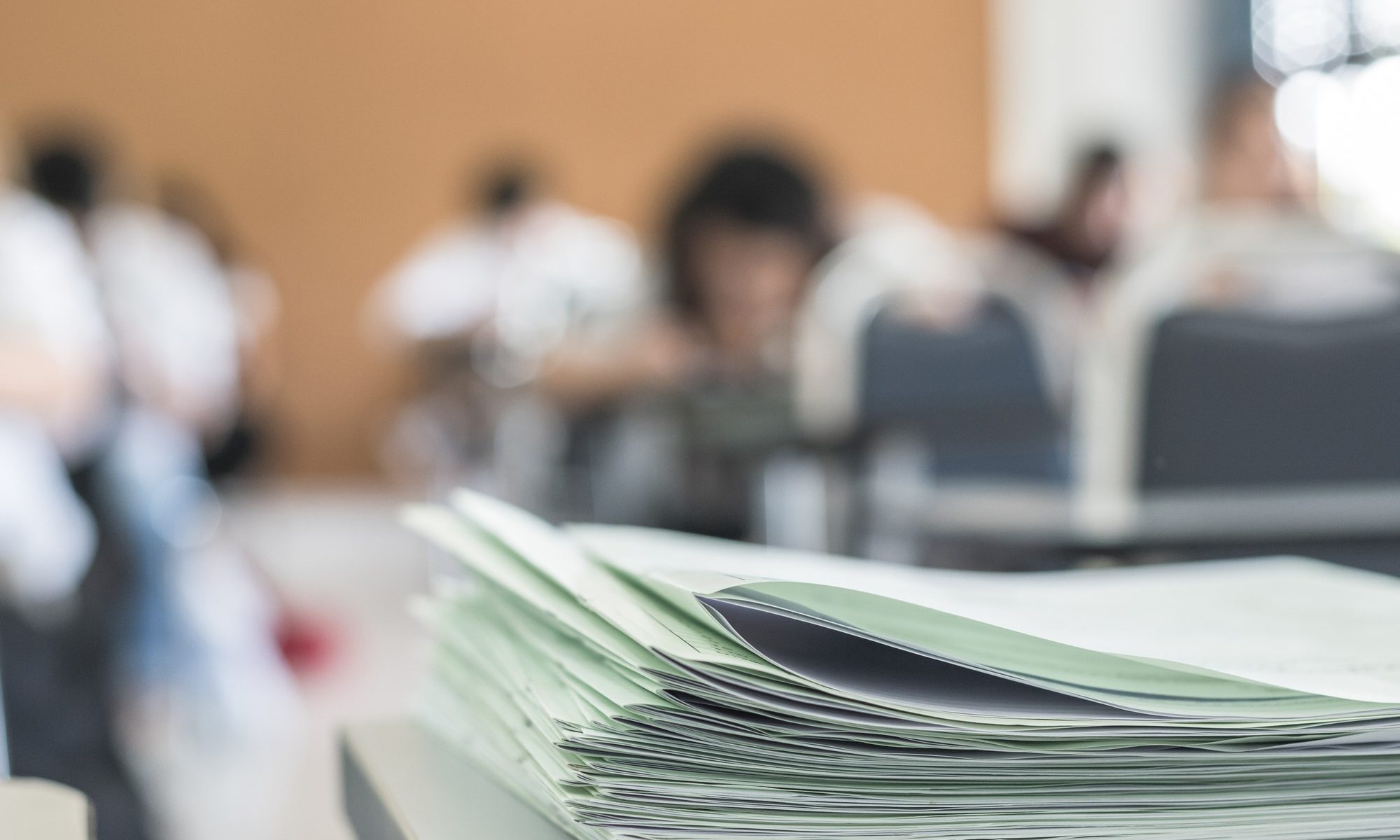 photograph of exams stacked on desk at front of class