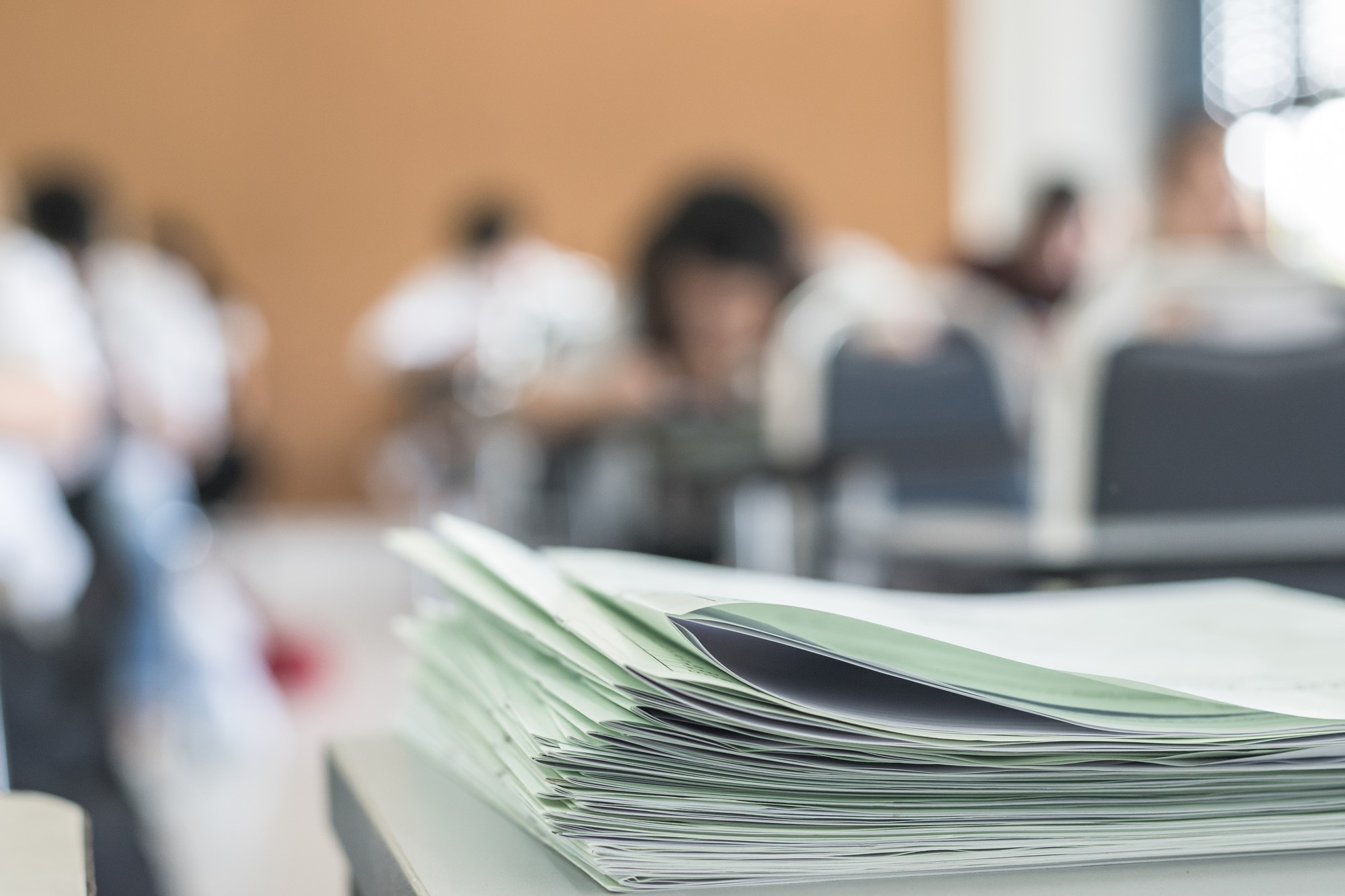 photograph of exams stacked on desk at front of class