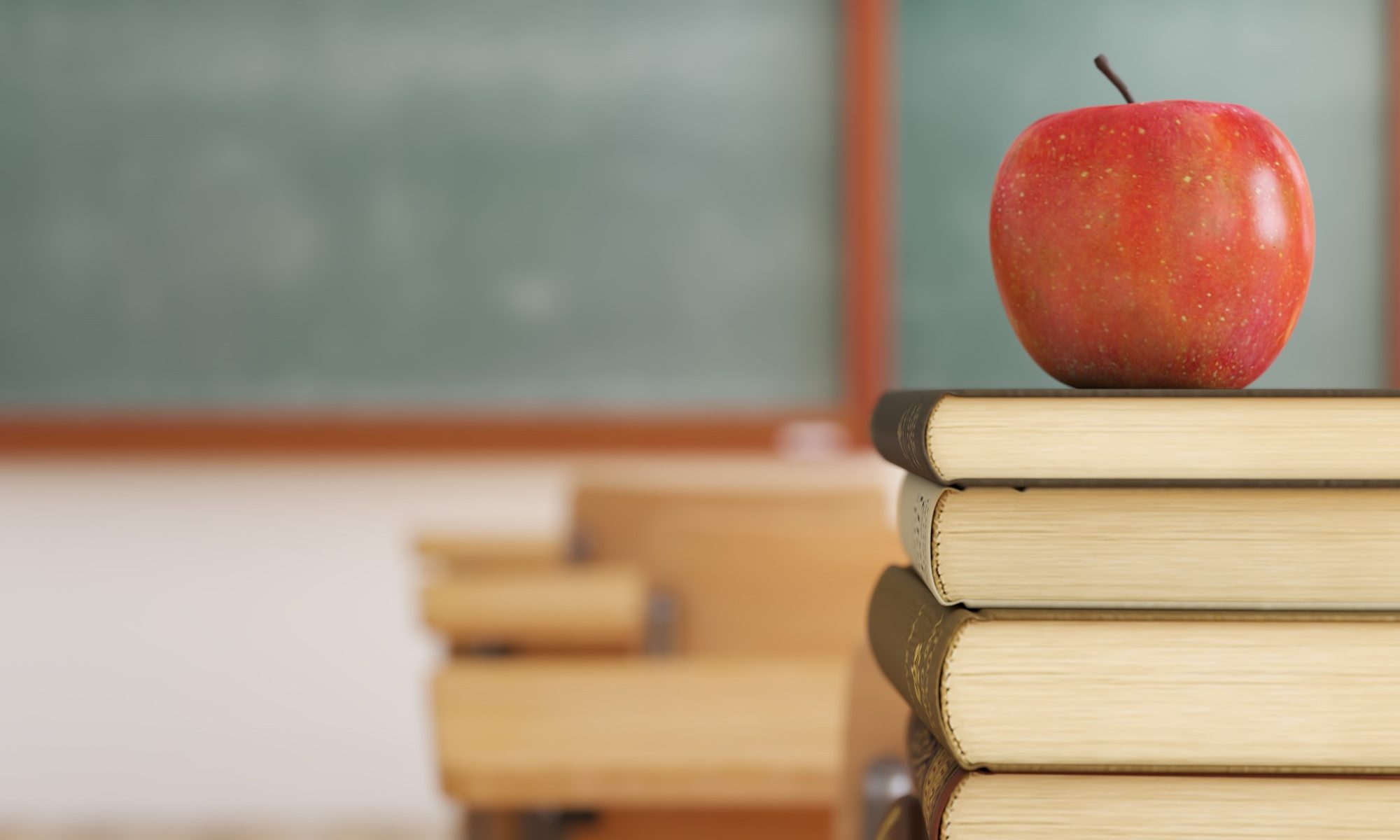 photograph of apple on top of school books stacked on desk