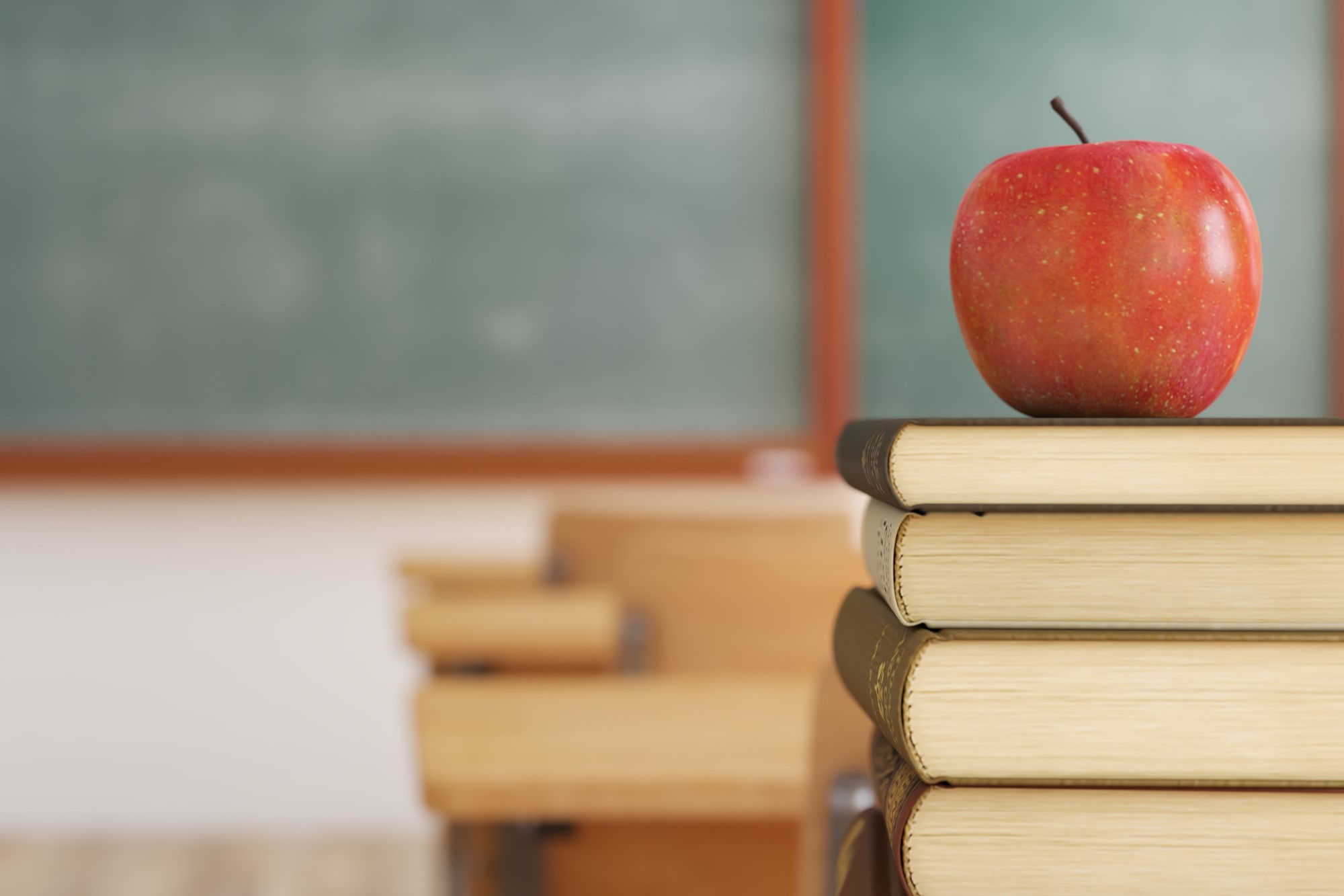 photograph of apple on top of school books stacked on desk