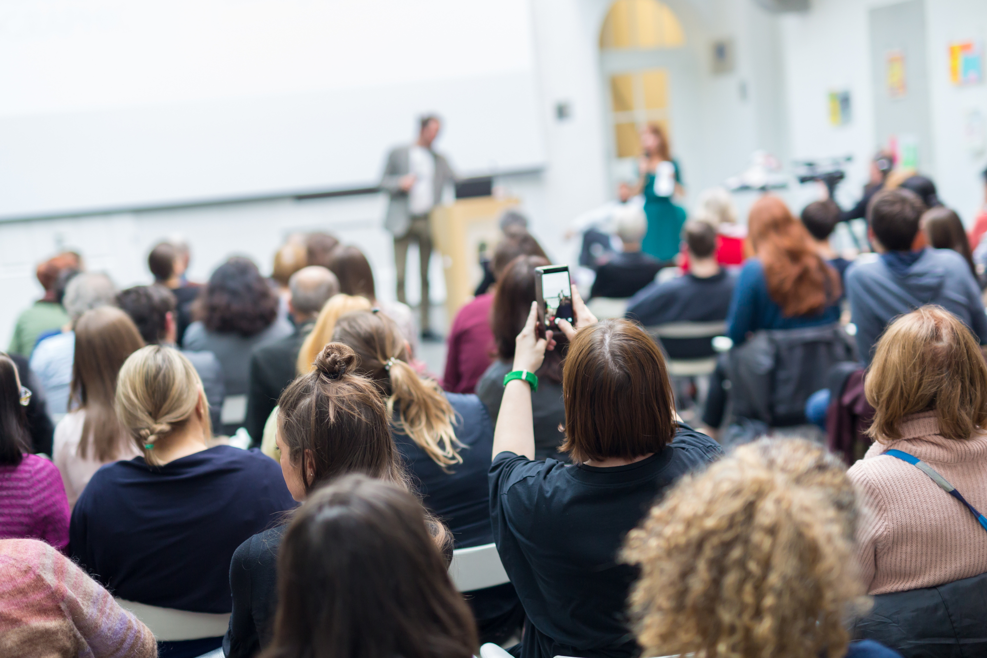 photograph of lecture with crowd member recording on her phone