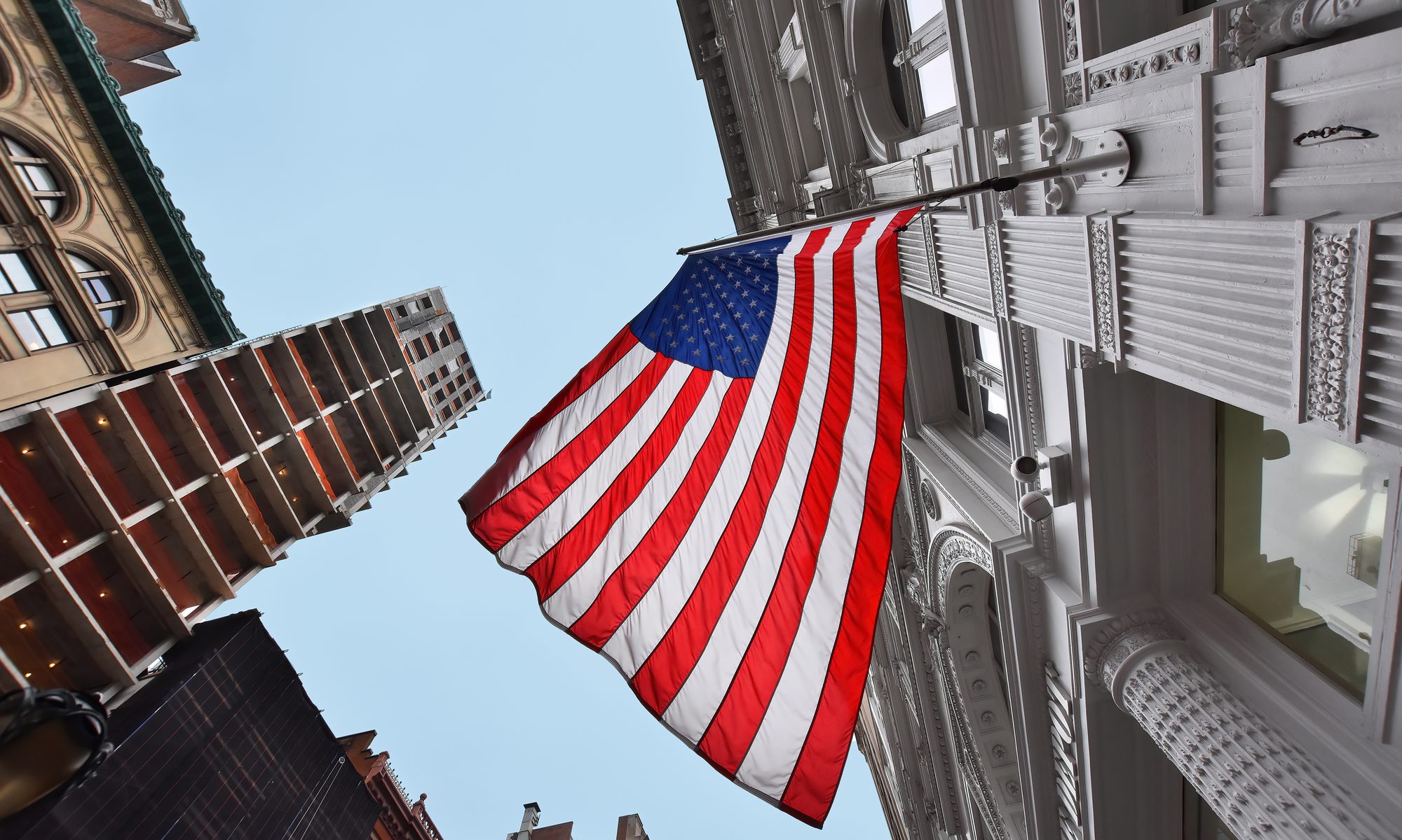 photograph of American flag hanging from tall buildings