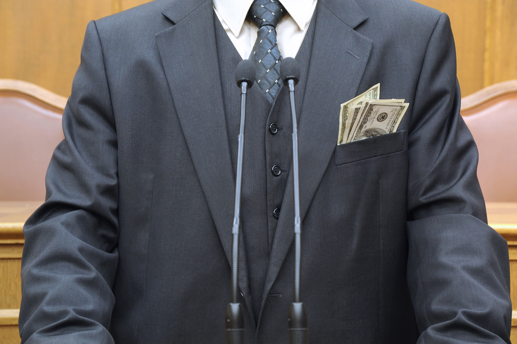 photograph of empty suit at podium with money hanging out of jacket pocket