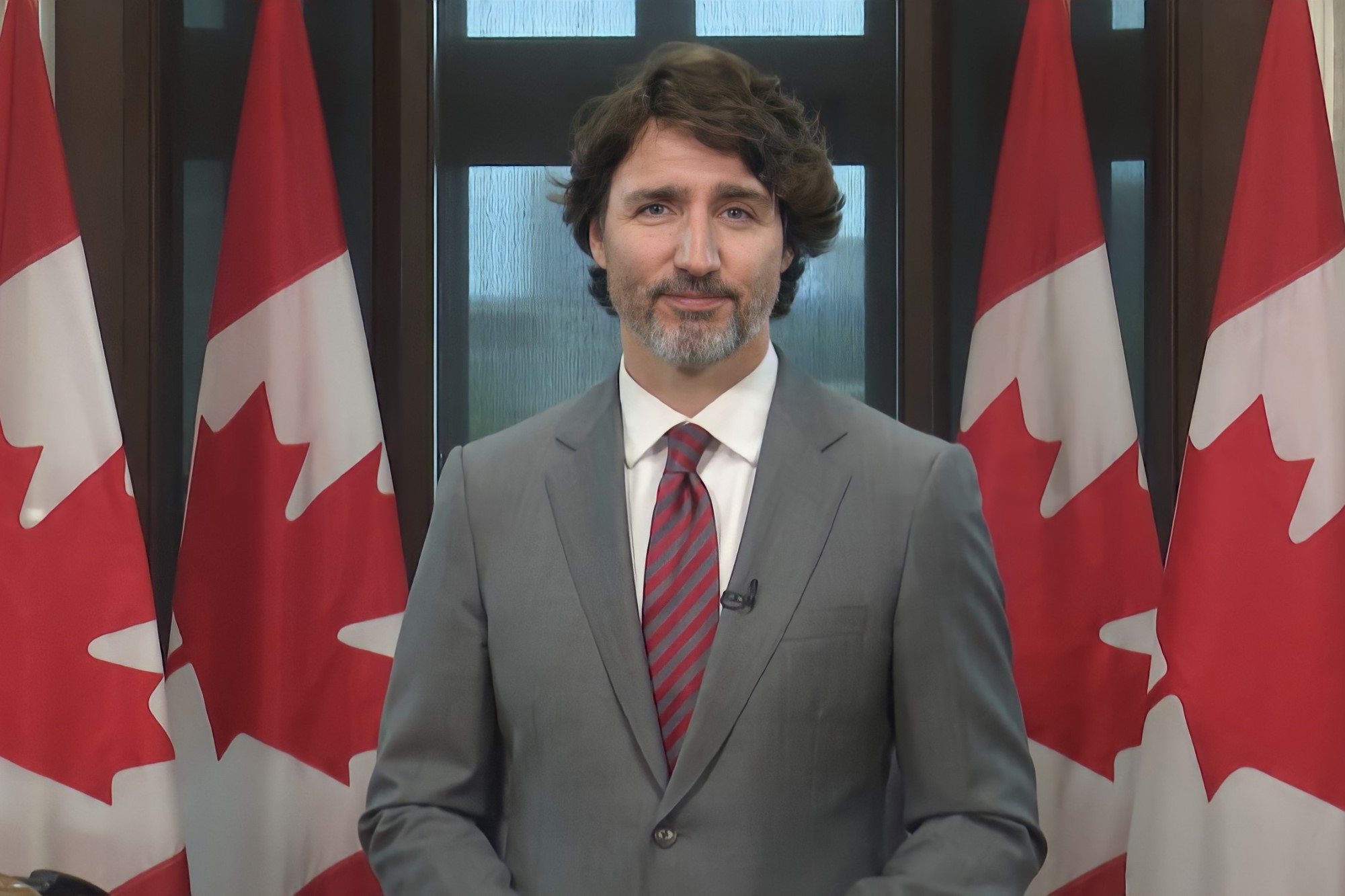 photograph of Justin Trudeau in front of row of Canadian Flags