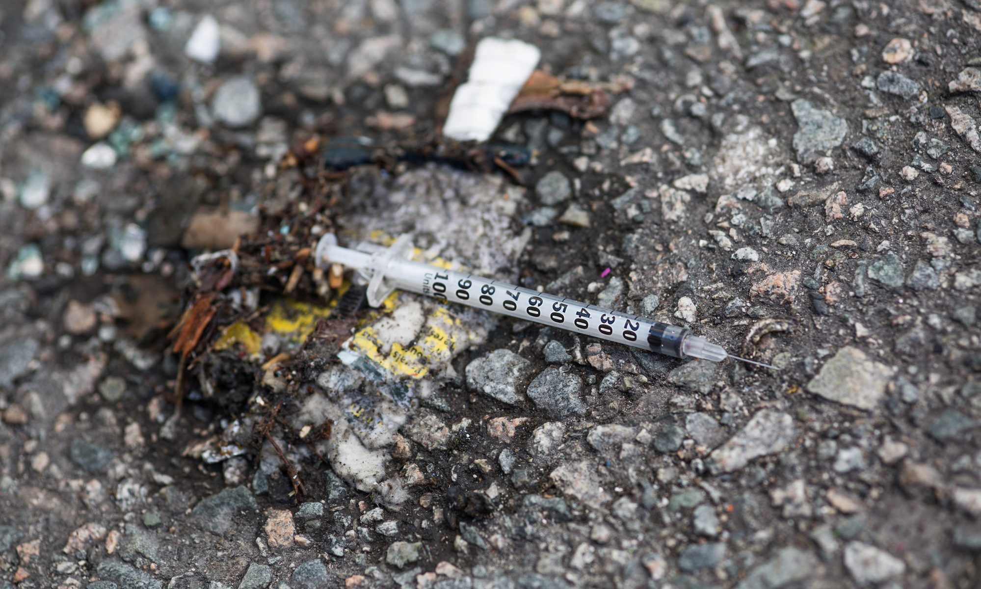 photograph of discarded syringe on asphalt