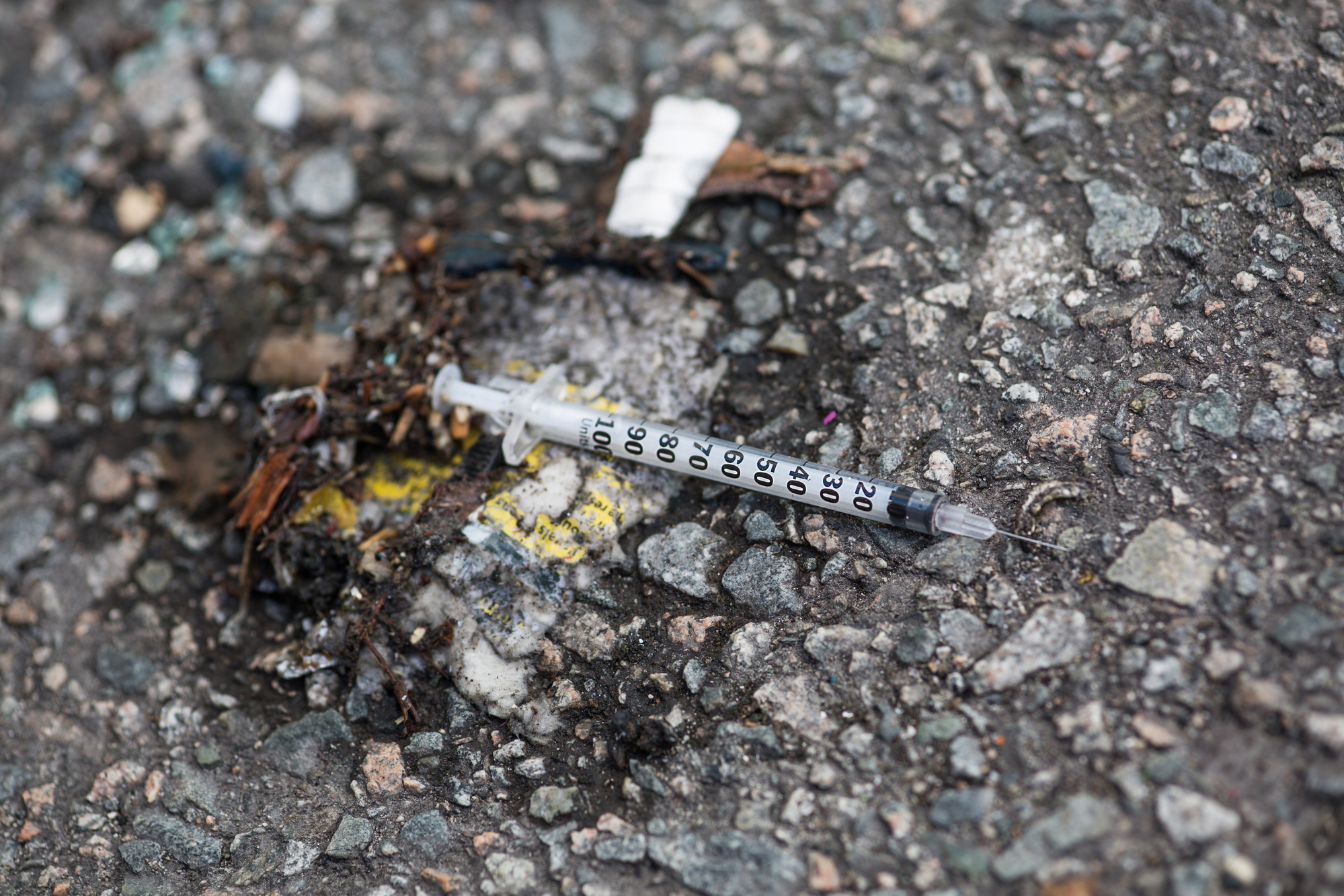 photograph of discarded syringe on asphalt