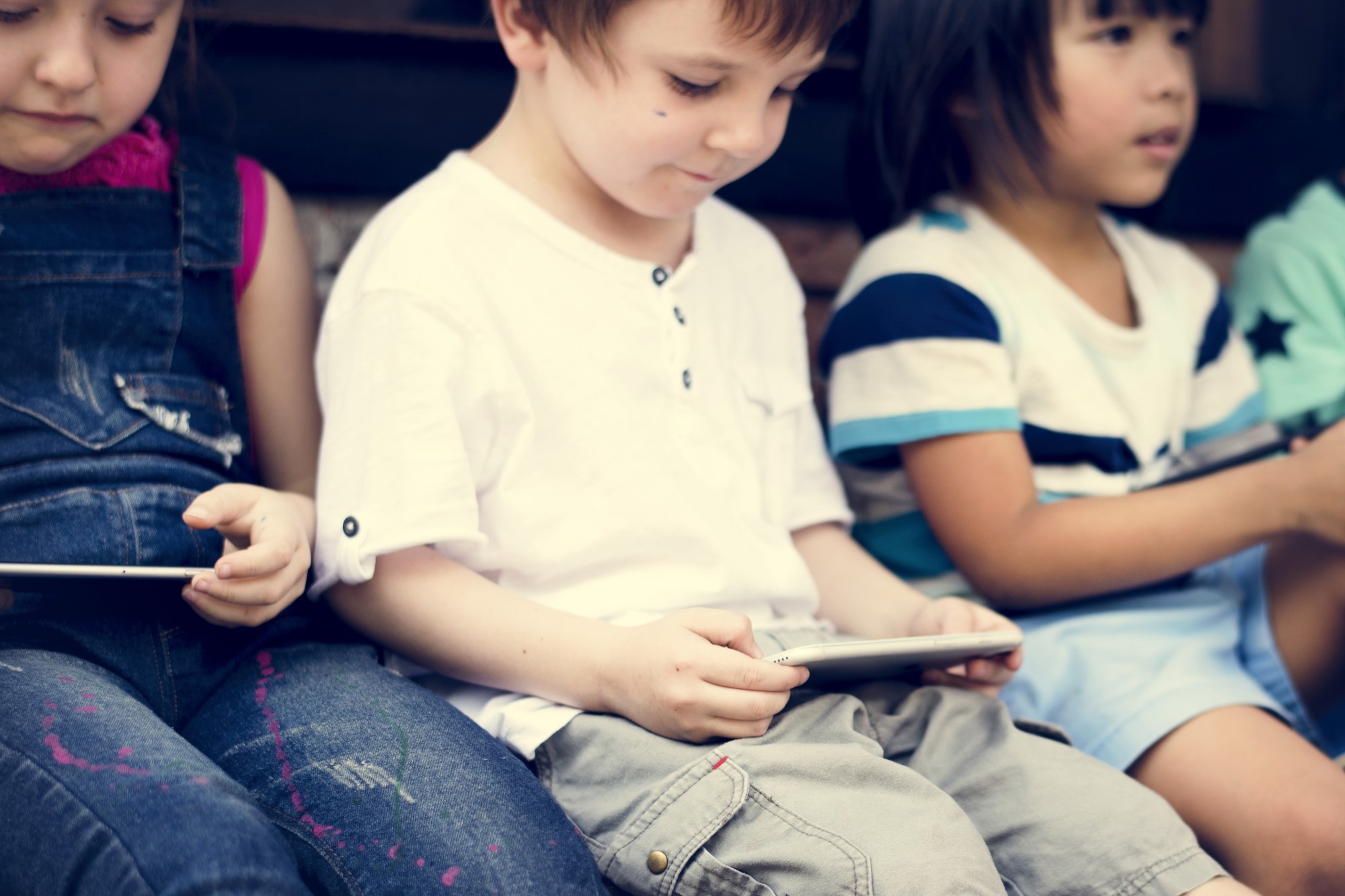 photograph of group of children using smartphones and tablets