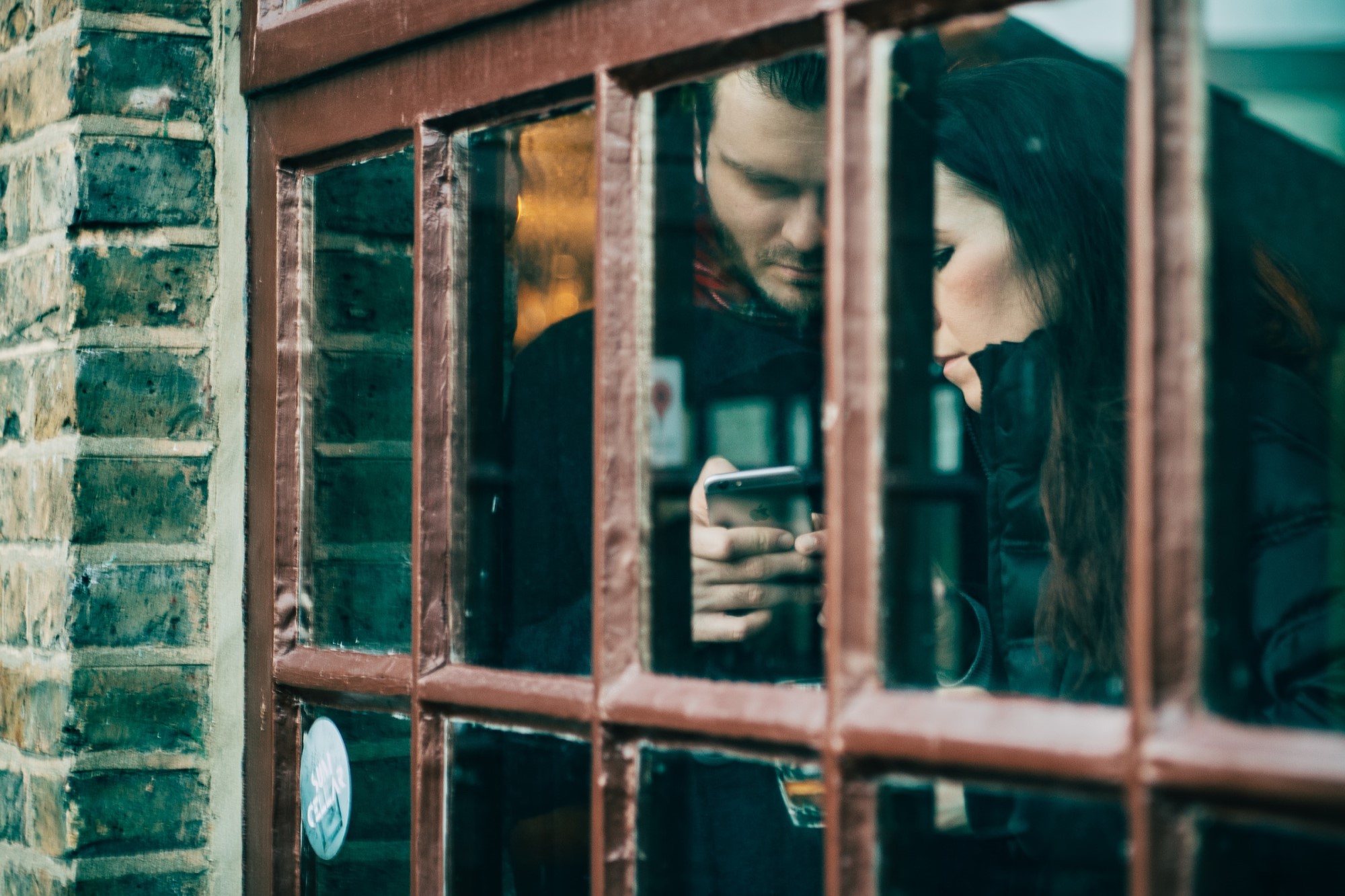 photograph of couple looking at smartphone behind window