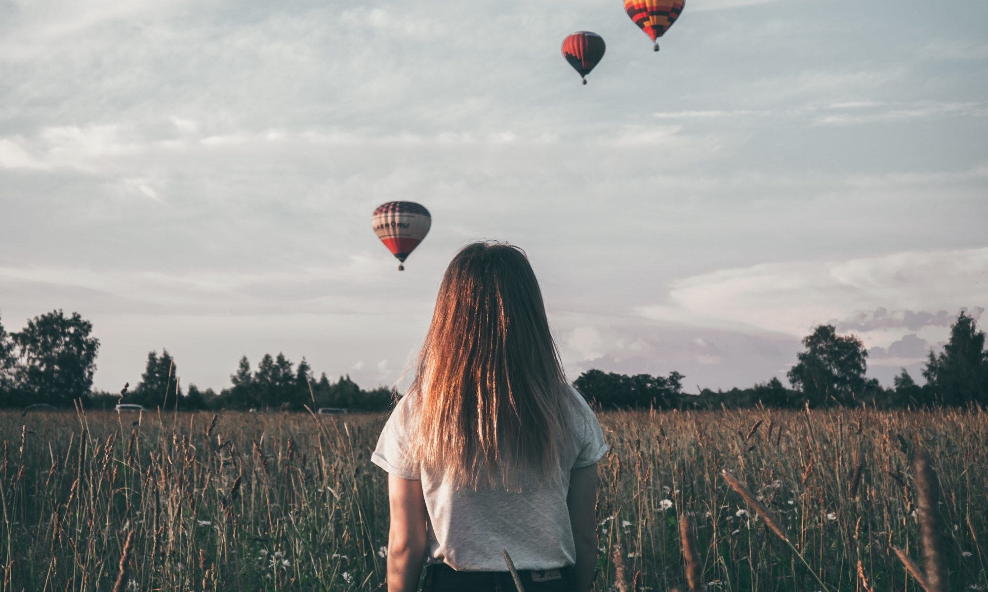 photograph of child standing in field watching hot air balloons