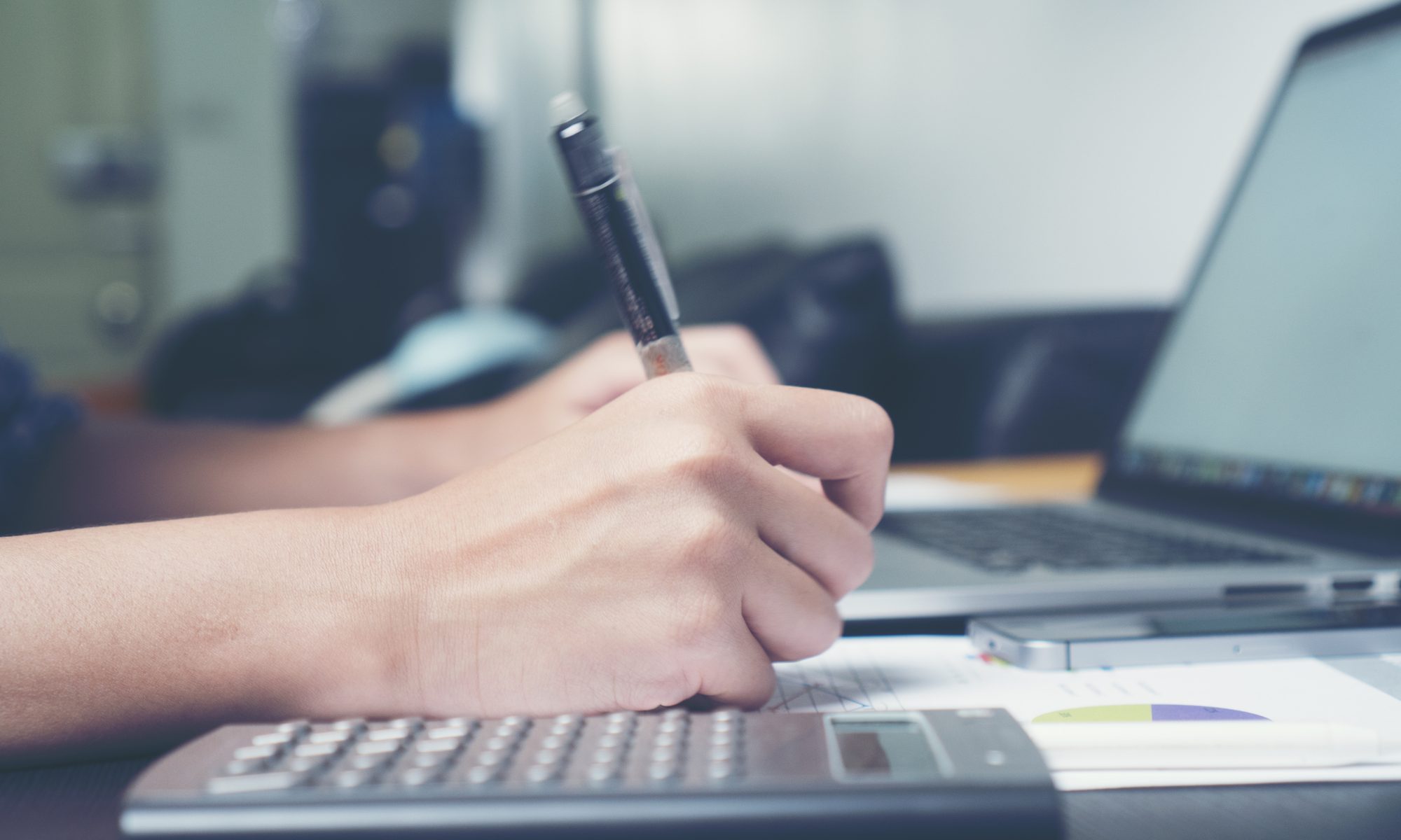 photograph of laptop and calculator with hands holding pen