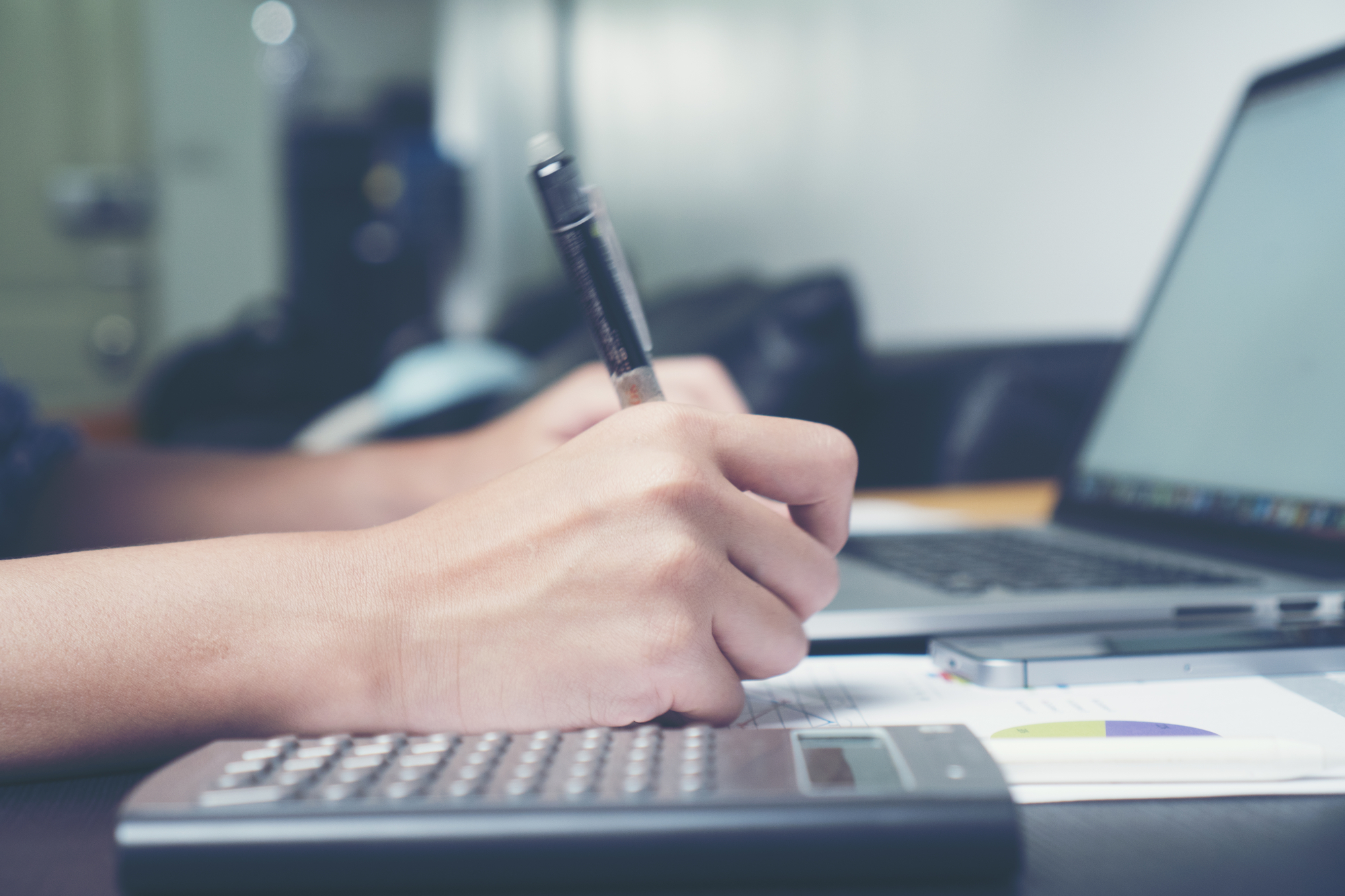 photograph of laptop and calculator with hands holding pen