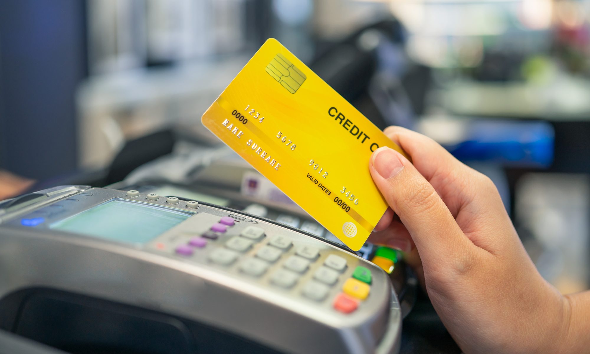 photograph of hand holding credit card over swipe machine