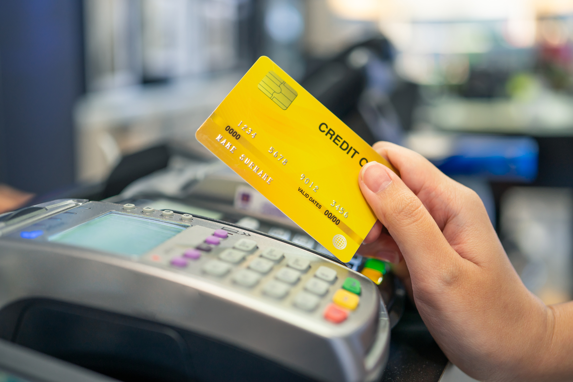 photograph of hand holding credit card over swipe machine