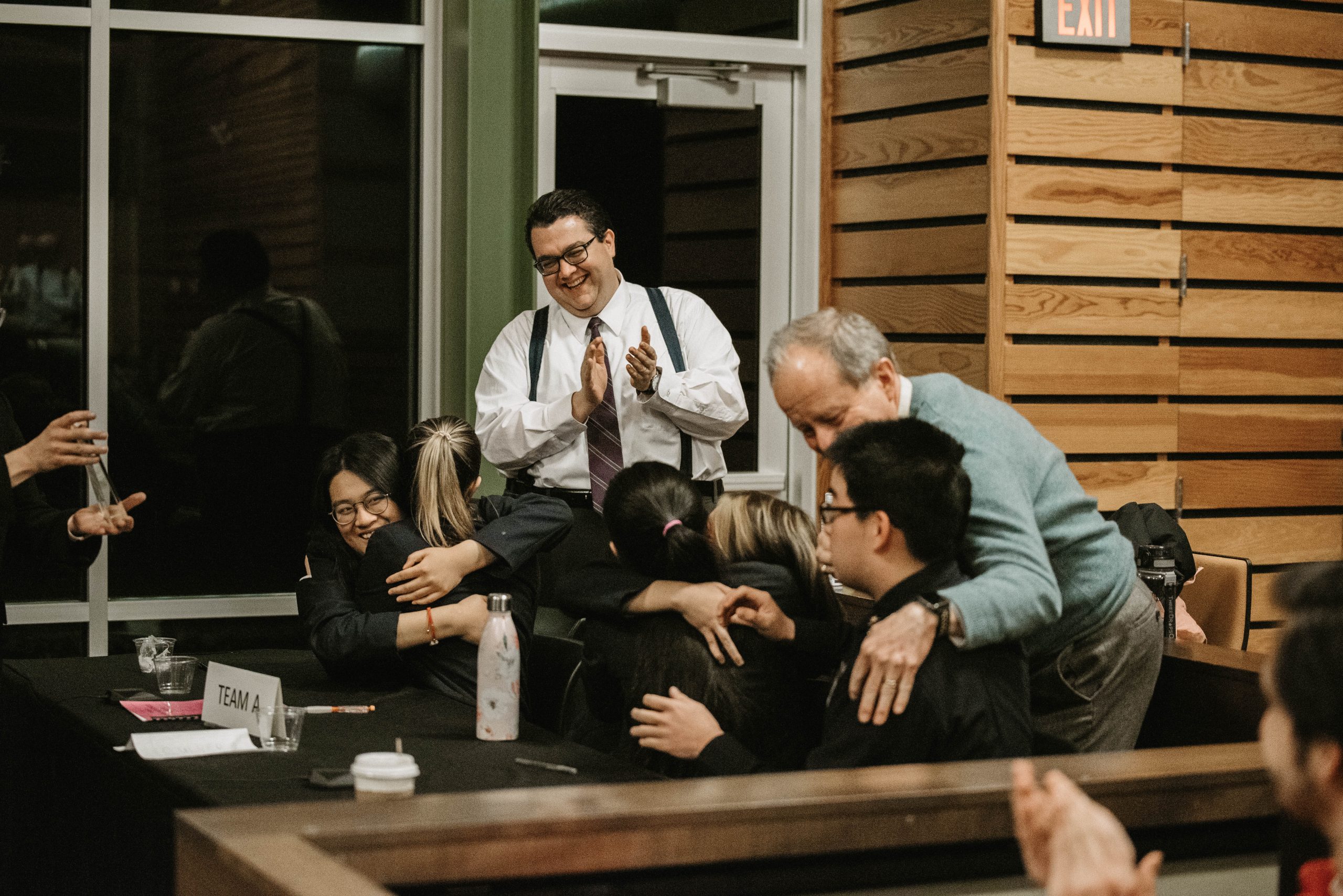 Group photograph of five high school students and two coaches embracing and clapping after winning the Indiana High School Ethics Bowl in 2023.