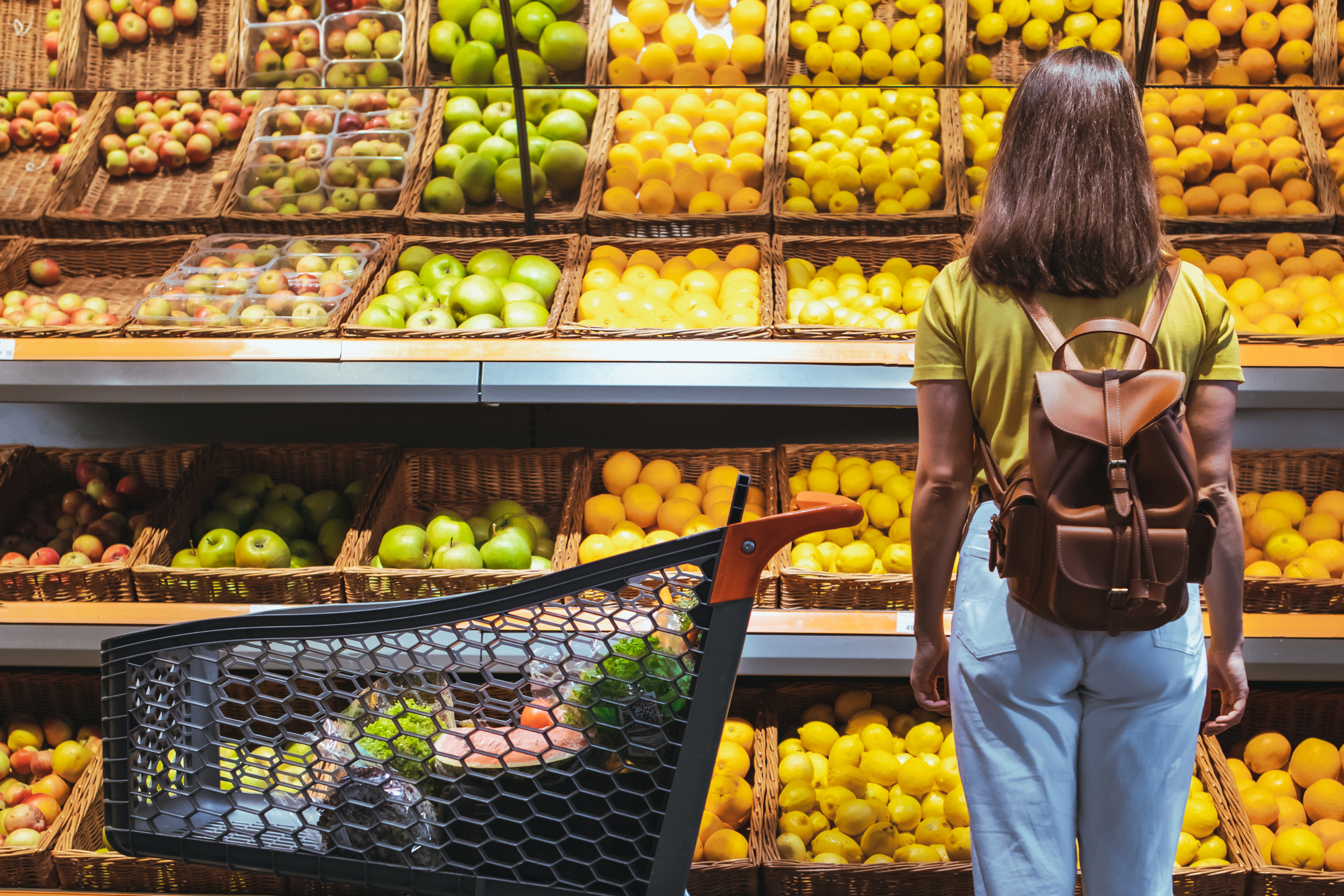 woman with backpack and cart standing in front of produce