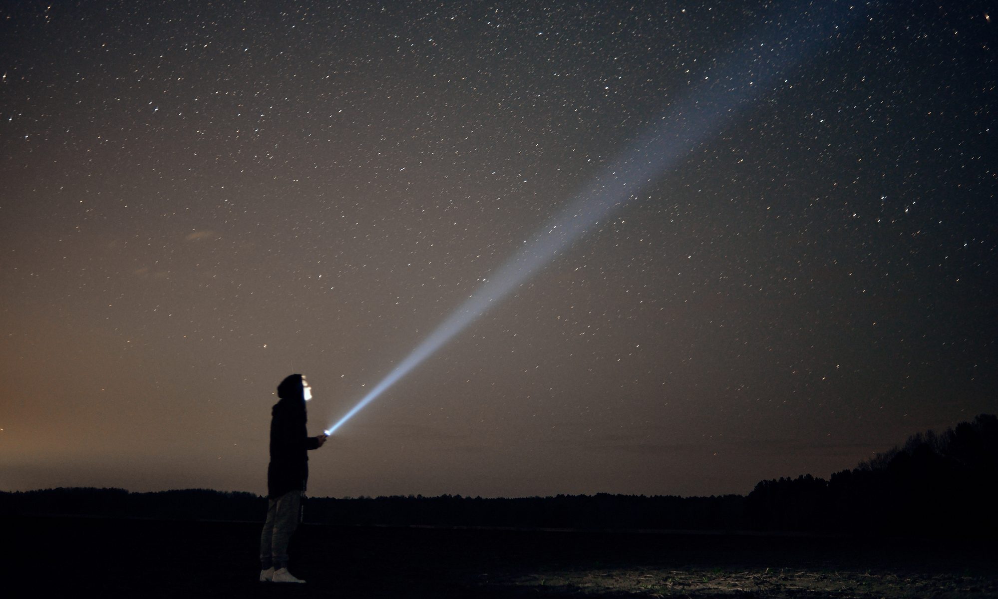 photograph of explorer with flashlight beam pointed to night sky