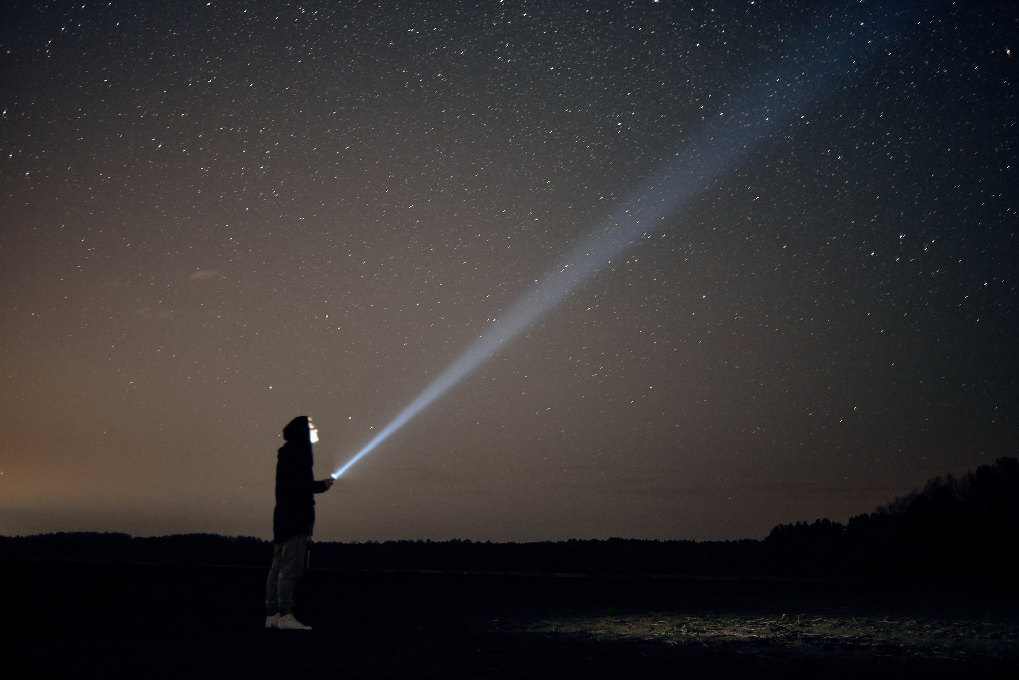photograph of explorer with flashlight beam pointed to night sky
