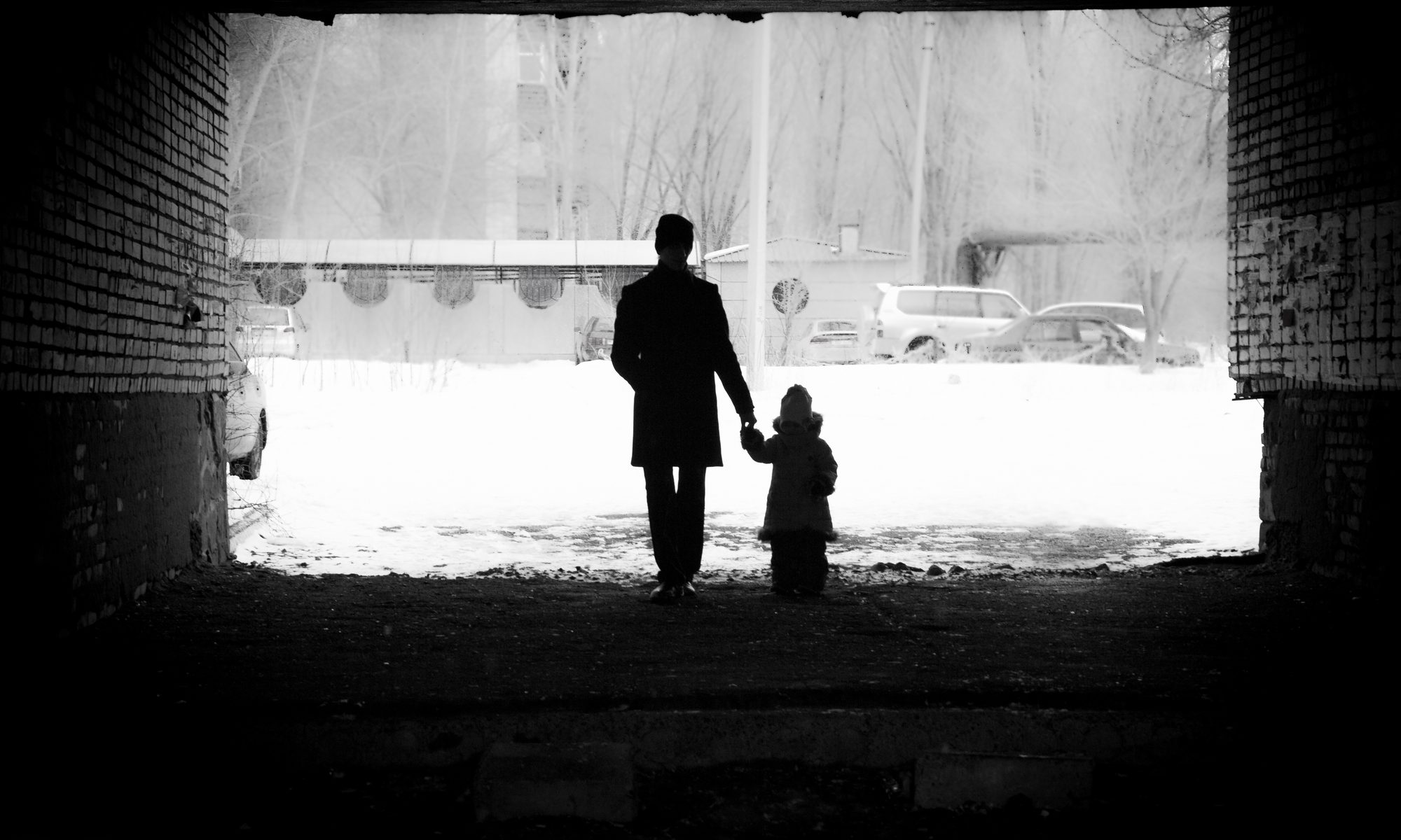 black and white photograph of parent and child holding walking through tunnel