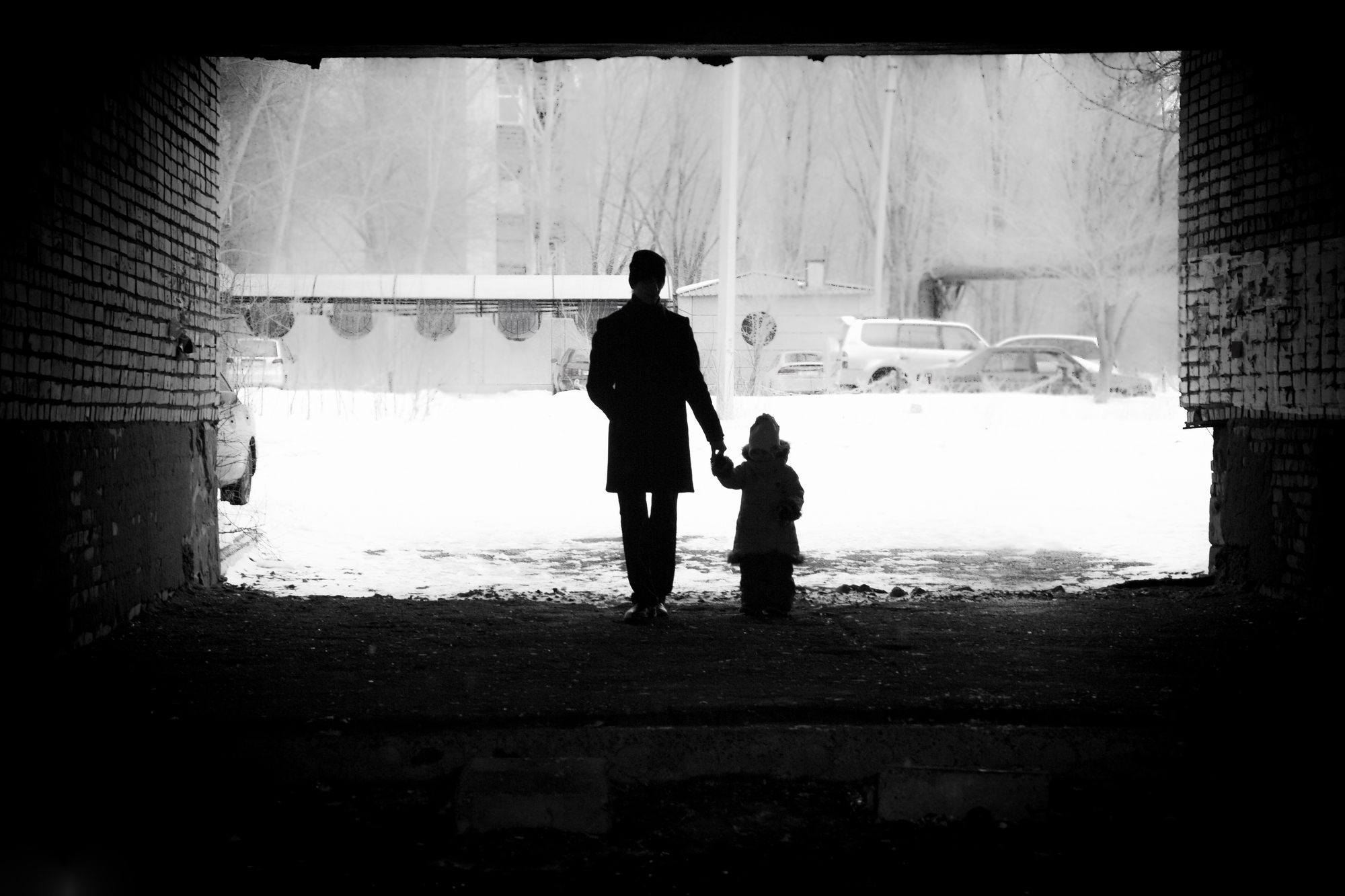 black and white photograph of parent and child holding walking through tunnel