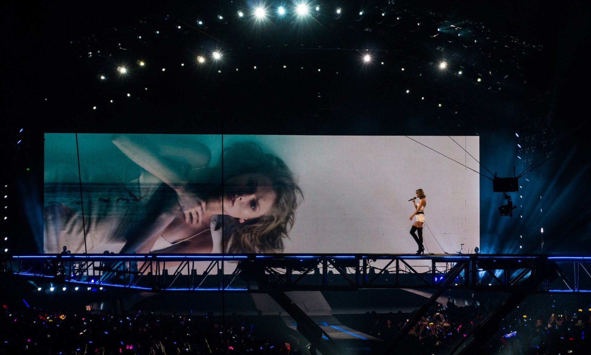 photograph of Taylor Swift performing on stage with image on screen in background
